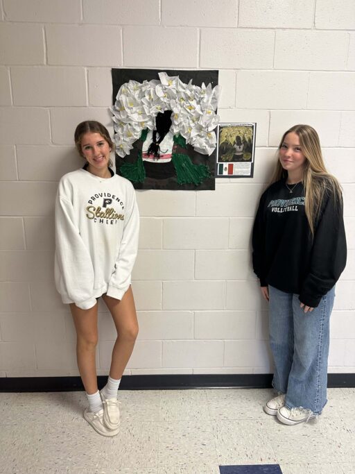 Two Hispanic students standing in front of a wall with Spanish artwork, reflecting Hispanic culture.